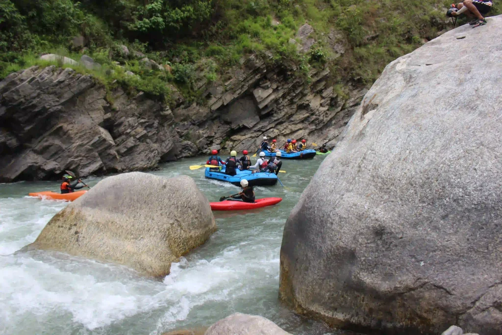 Kayakers and rafting groups navigate a rocky river with strong rapids