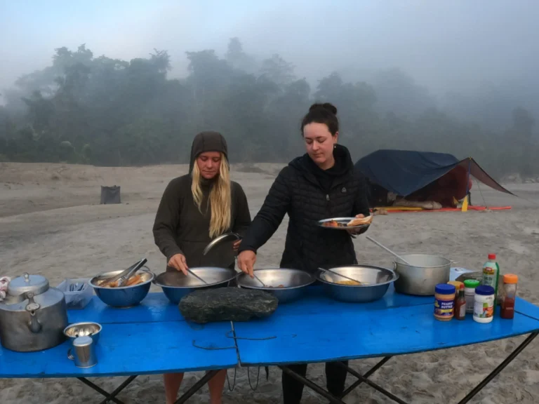 People serving breakfast at a riverside campsite